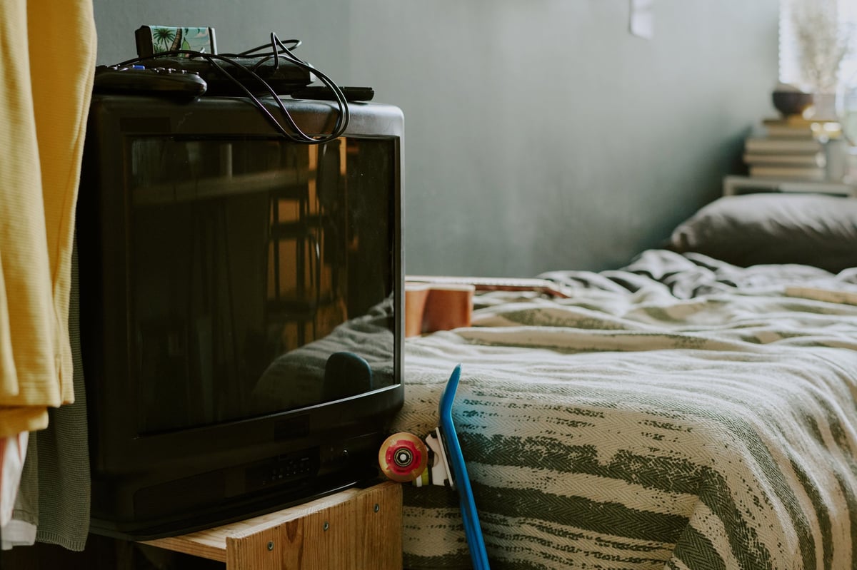 Medium close up of retro TV with console on top, single bed covered with striped linen