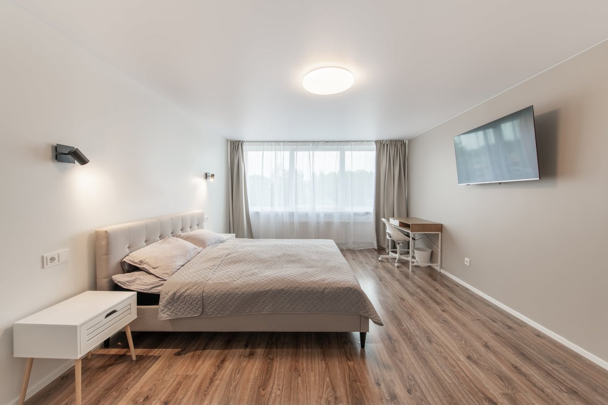Luxurious master home bedroom interior, modern house, beautiful interiors, wide bedroom. TV Set on the Wall. King Size Bed, White Walls and Ceiling. Hardwood Floor. Wide Angle