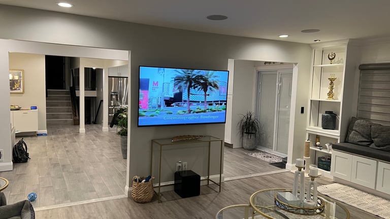 Modern living room with mounted TV showing beach scene, light gray walls, white cabinetry, and contemporary furnishings