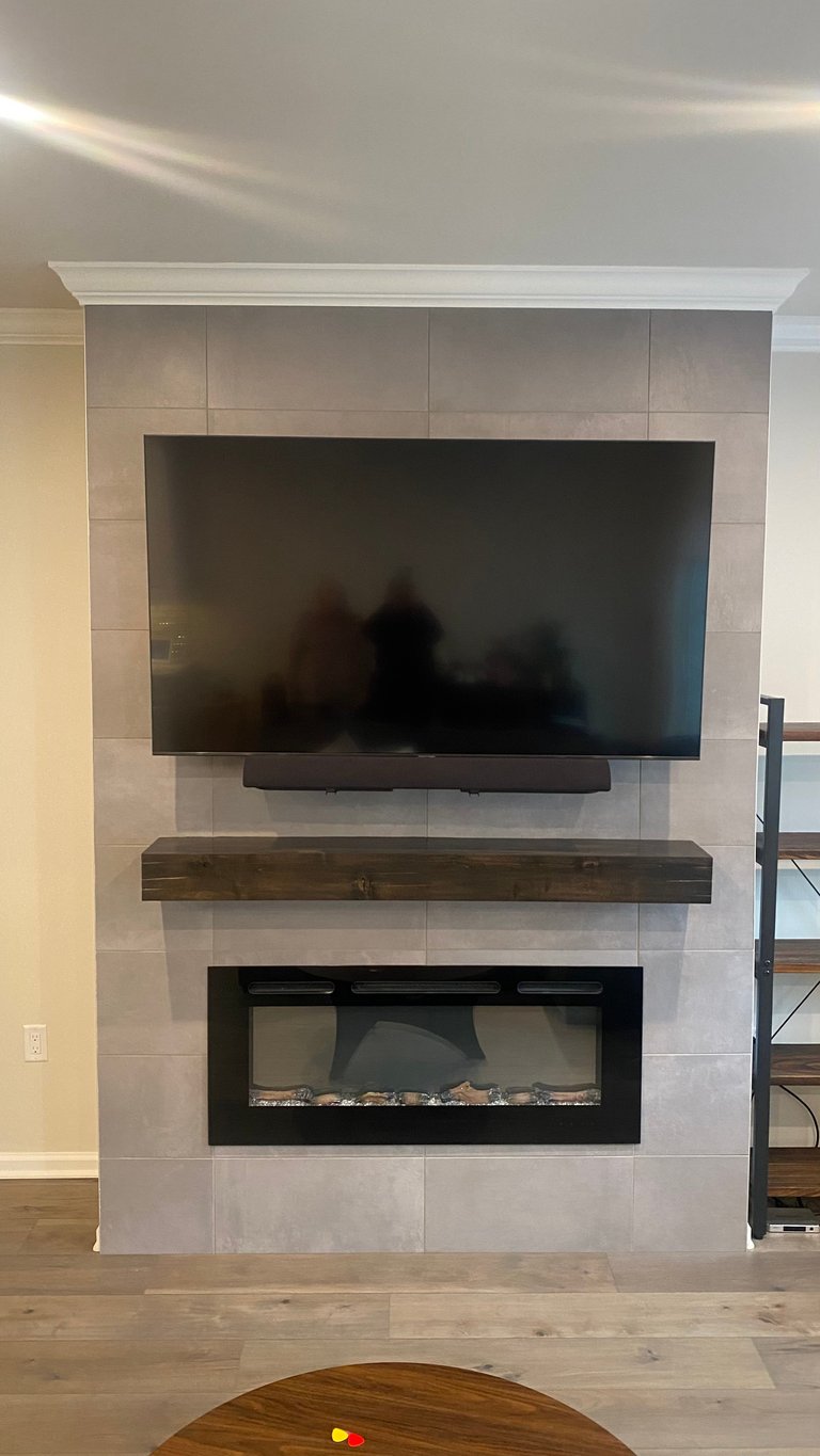 Modern fireplace feature wall with mounted TV above wooden mantel and electric fireplace insert below, tiled surround